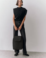 Person in sleeveless top and jeans holding a backpack.