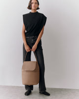 Person standing with a leather backpack, wearing a sleeveless top and jeans.