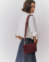 Person wearing a skirt and shirt, holding a shoulder bag.