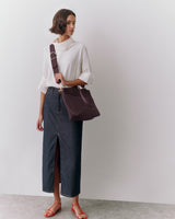 Person with shoulder bag, wearing a long skirt and sandals, looking to the side.