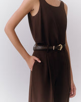 Person wearing sleeveless top and trousers with a belt. Hand in pocket.