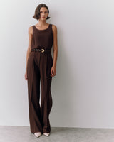 Person wearing sleeveless top, wide-leg pants, and a belt with buckle, standing against a wall.