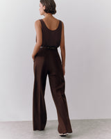 Person in a sleeveless top and wide-leg pants standing against a plain backdrop.