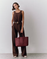 Person wearing a sleeveless top and pants, holding a tote bag.