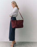 Person standing side view holding a tote bag wearing a shirt and long skirt with heels.