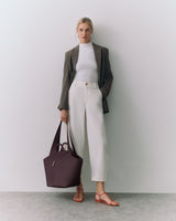 Person stands with a handbag, wearing a jacket, top, and pants.