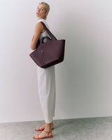 Person standing with large tote bag, wearing sleeveless outfit and sandals.