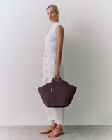 Person standing, holding a large handbag, wearing a sleeveless top and pants with sandals.