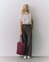 Woman stands holding a large tote bag, wearing a sleeveless top and wide-leg pants.