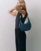 Person holding purse on shoulder, wearing sleeveless top and pants.