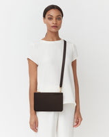 Person wearing a shirt with crossbody bag standing against plain background.