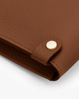 Close-up of textured leather laptop sleeve with metallic ring detail.