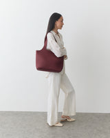 Person stands sideways with large bag on shoulder.