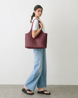 Person standing with large tote bag, wearing jeans and sandals.