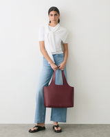 Person wearing jeans, a top, and sandals, holding a large handbag.