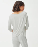 Woman standing, seen from behind, wearing a long sleeve top and pants.