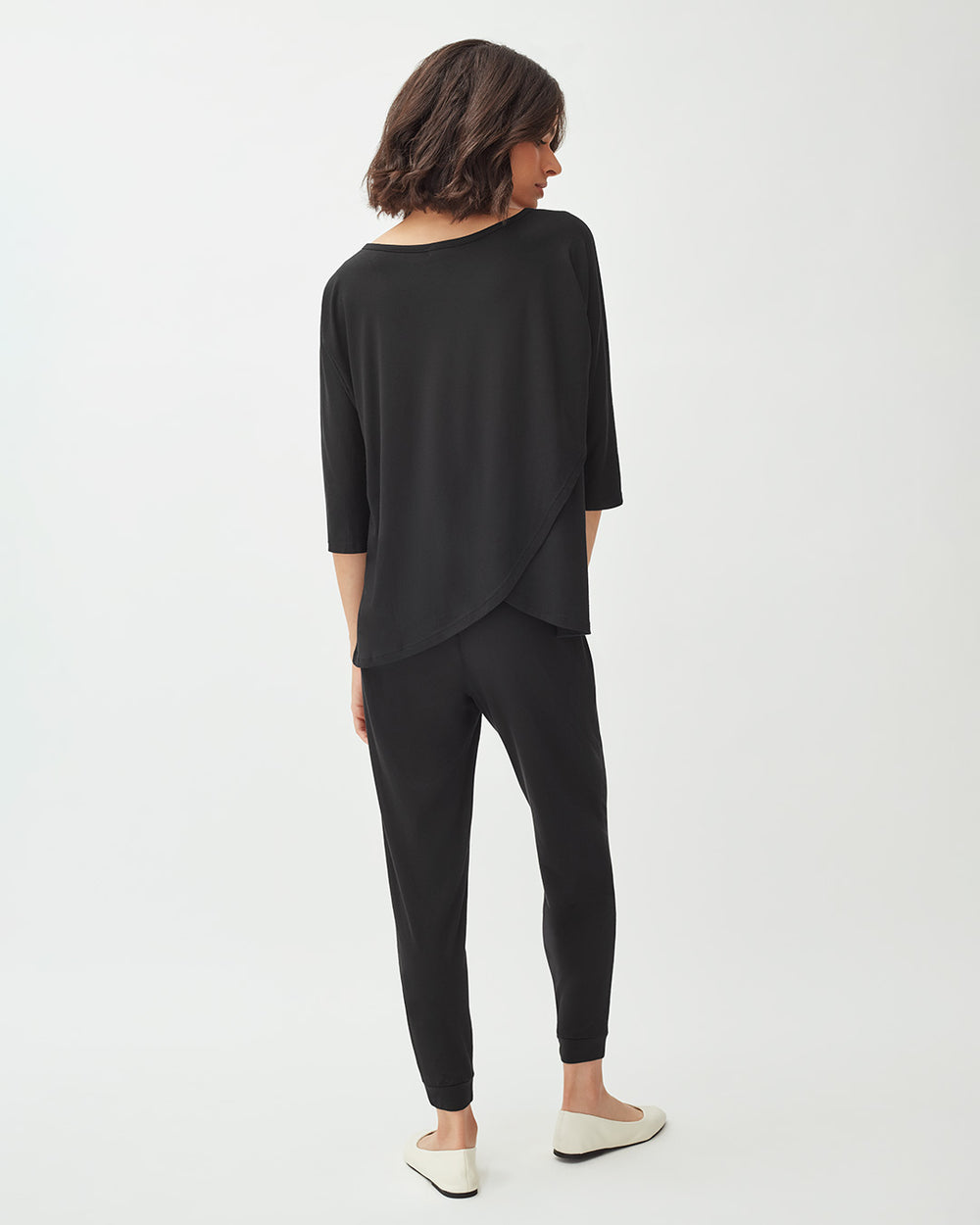 Woman in an outfit with pants and a draped top, viewed from behind.