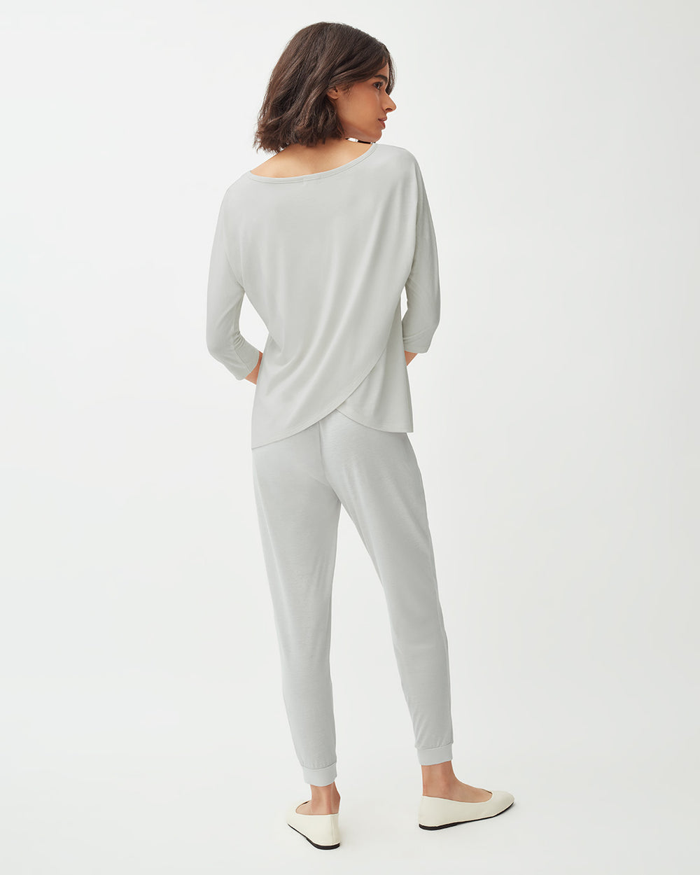 Woman viewed from behind, standing in a relaxed pose wearing casual attire.