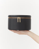 Hand holding a small round zipped case against a plain background.