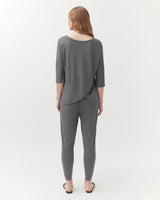 Woman standing facing away, wearing a top and trousers, in a studio setting.