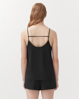 Woman standing with her back facing the camera, wearing a tank top with thin straps.