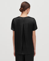 Woman viewed from behind with hair in a bun wearing a top with a split back design.