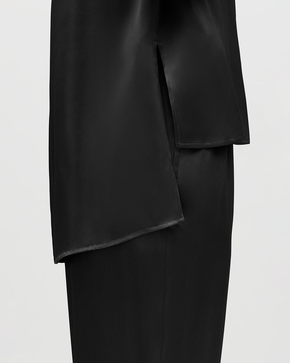 Close-up of a skirt with asymmetric hem over trousers.