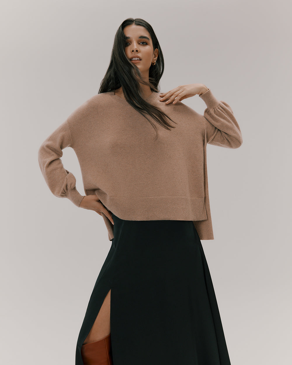 A woman in a sweater and long skirt posing with one hand on her neck.