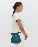 Profile view of a woman standing with a handbag on her shoulder.