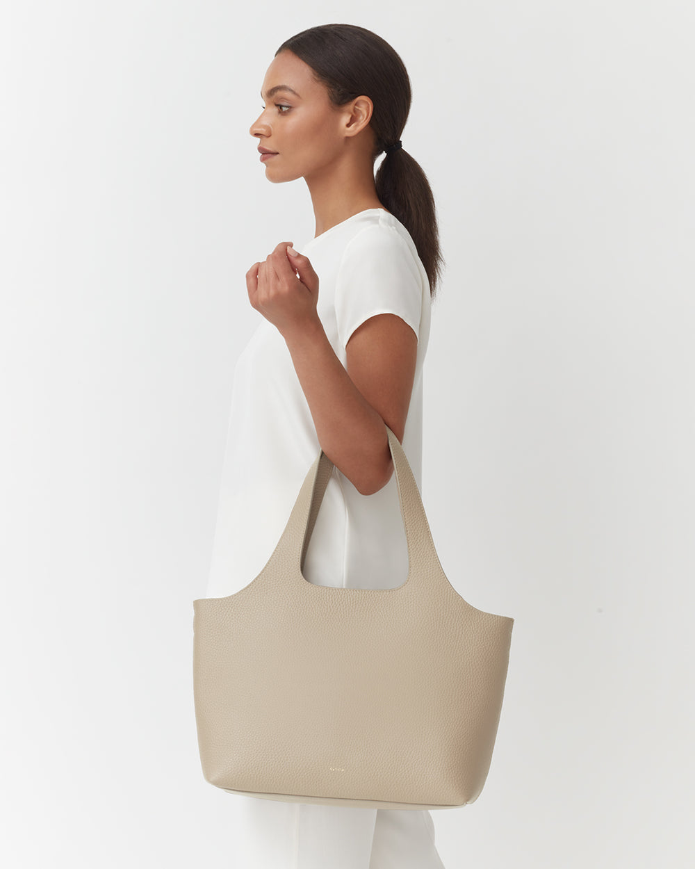 Woman standing sideways holding a large handbag.