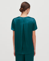 Woman facing away with a bun hairstyle, wearing a blouse and pants.