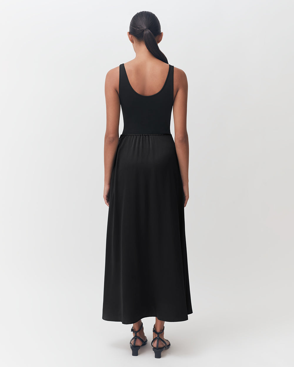 Woman standing in a dress and heels, viewed from the back.