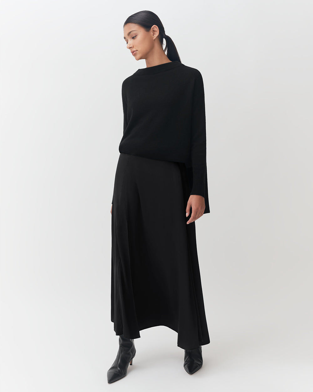 Woman standing in a long-sleeved top and flowing pants with ankle boots.