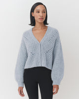 Woman wearing a V-neck sweater and pants, standing and facing forward.
