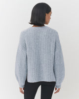 Woman facing away, wearing a sweater and black pants.