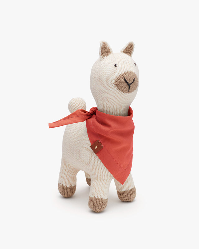 Stuffed toy alpaca with a bandana around its neck standing against a solid background.