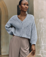 Woman in sweater and trousers standing by a textured wall