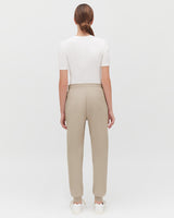 Woman standing with her back to the camera, wearing a top and pants.