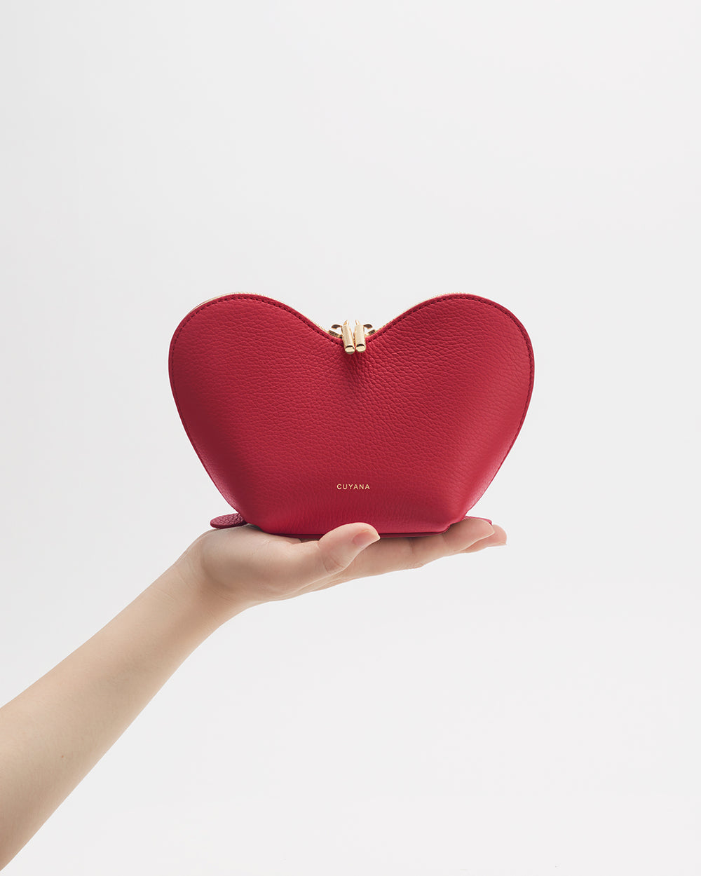 Hand holding a heart-shaped purse against a plain background.