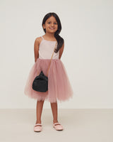 Young girl standing and smiling with a handbag and fluffy skirt.
