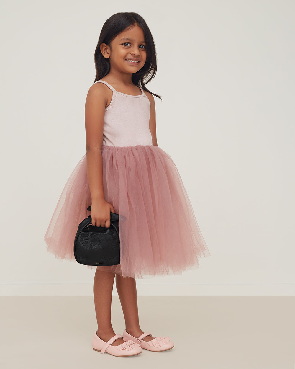 Young girl in a tutu and ballet flats holding a handbag.