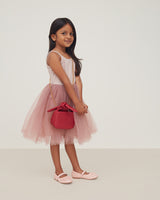 Young girl in a dress holding a purse, standing and looking at the camera.