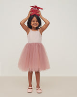 Young girl in a dress, balancing a gift on her head, smiling.
