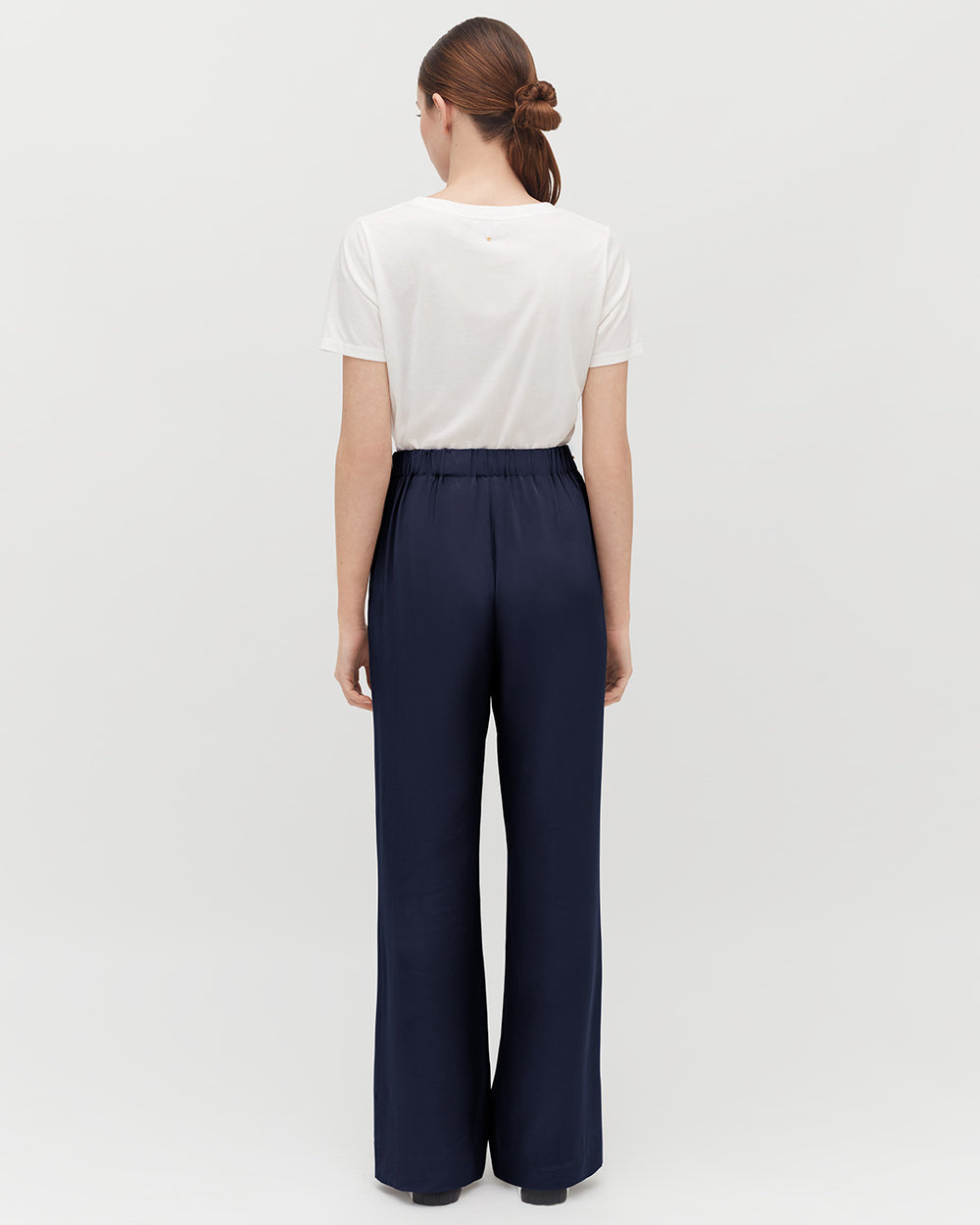 Woman standing with her back facing the camera wearing a T-shirt and wide-leg pants
