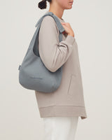 Person standing sideways holding a backpack over one shoulder.