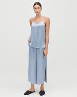 Woman standing in a sleeveless top and long pants with side slit.
