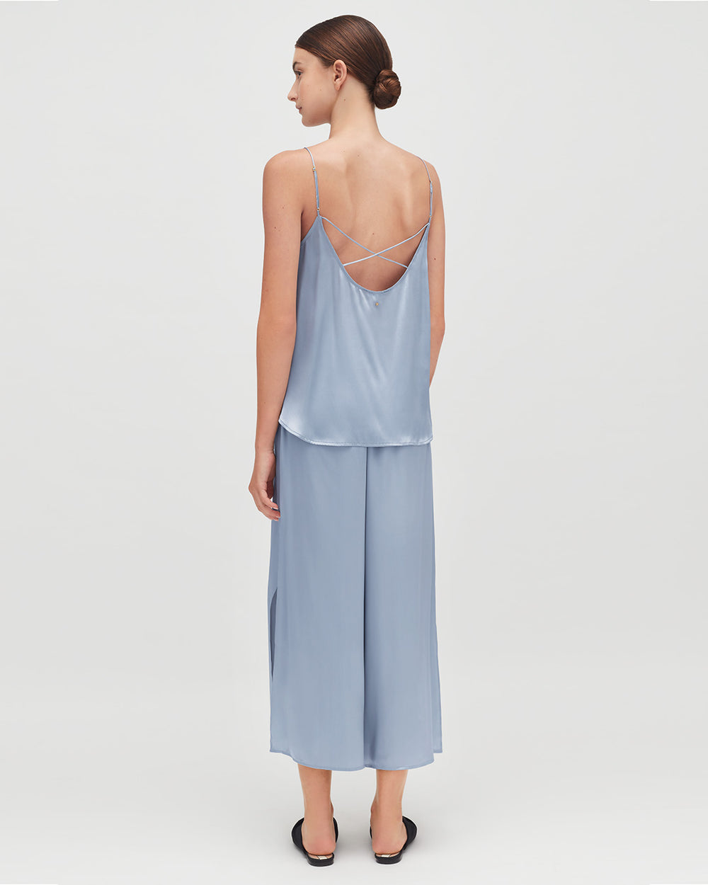Woman standing, seen from behind, wearing a top and long skirt with crisscross straps.