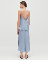 Woman standing, seen from behind, wearing a top and long skirt with crisscross straps.