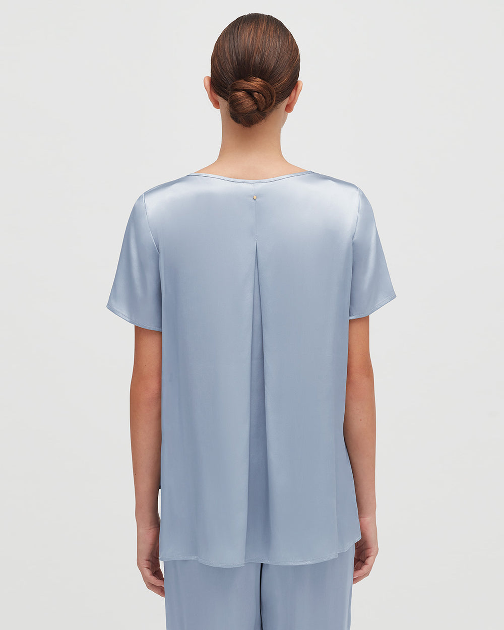 Woman with hair in a bun, viewed from behind, wearing a blouse with a split back design.