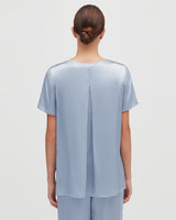 Woman with hair in a bun, viewed from behind, wearing a blouse with a split back design.